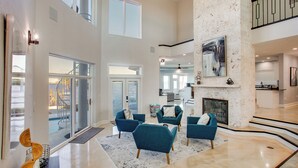 A spacious living area with a high ceiling, a fireplace, and a view of the outdoors. - Riverfront Fort Myers Luxury Home w/ Heated Pool! (Fort Myers)