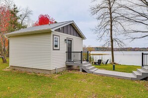 A small cabin with a porch and steps leading to a dock by a lake.