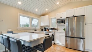 A modern kitchen with white cabinets, a stainless steel refrigerator, and a bar area with black stools. - Fish, Swim & Explore! 2-cabin Camp on Round Lake (Luck)