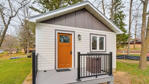A small, single-story house with a front porch, a wooden door, and a window. - Fish, Swim & Explore! 2-cabin Camp on Round Lake (Luck)