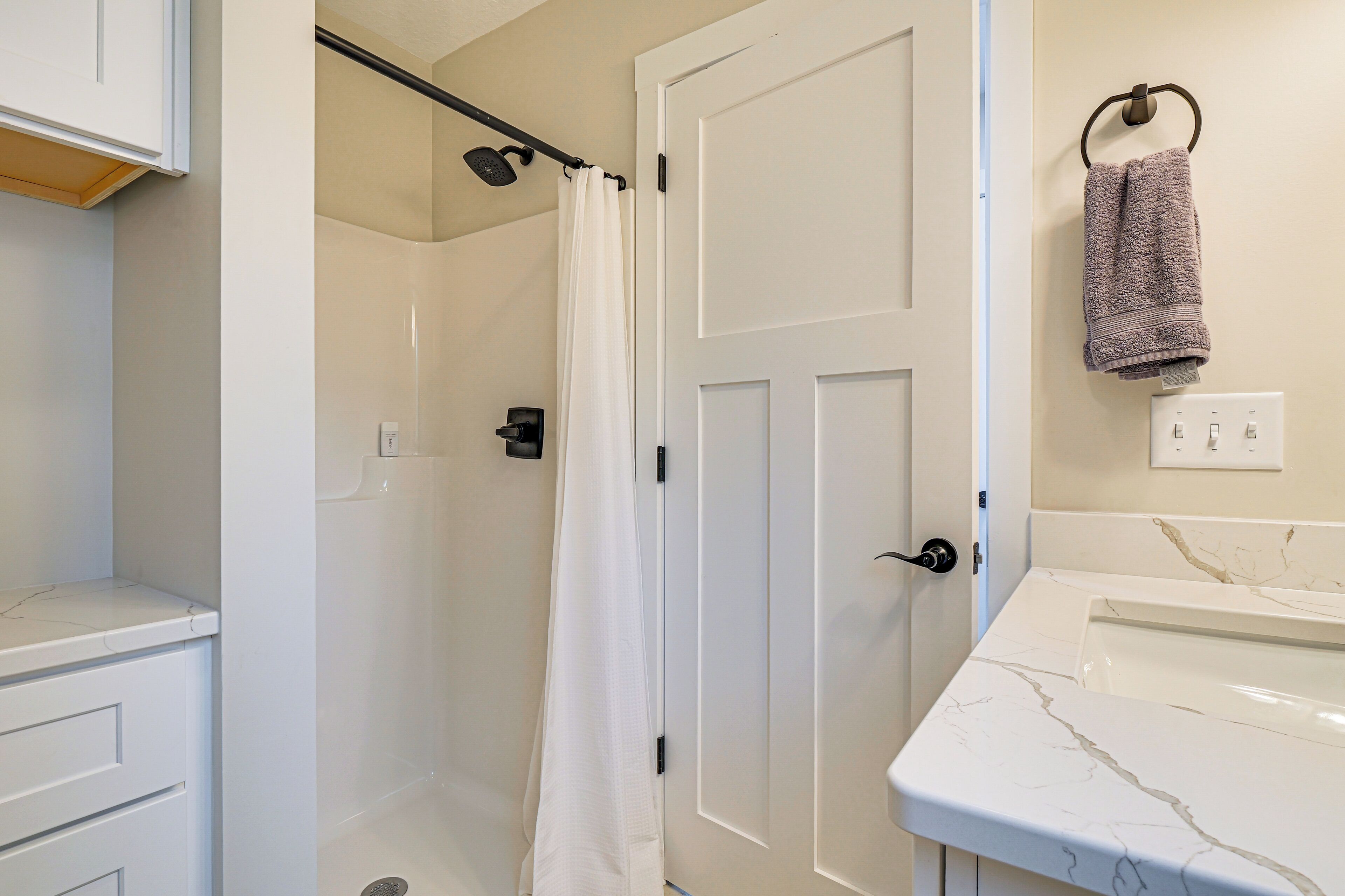 A bathroom with a shower, a white door, a marble sink, and a towel hanging on a hook.
