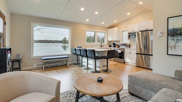 A modern kitchen with a large island, bar stools, and a view of a lake. - Fish, Swim & Explore! 2-cabin Camp on Round Lake (Luck)