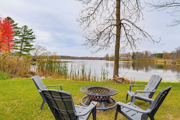 A lakeside outdoor seating area with Adirondack chairs and a circular fire pit.