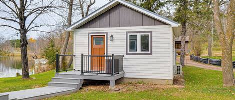 A small, single-story cabin with a wooden door and a small porch with a black railing.