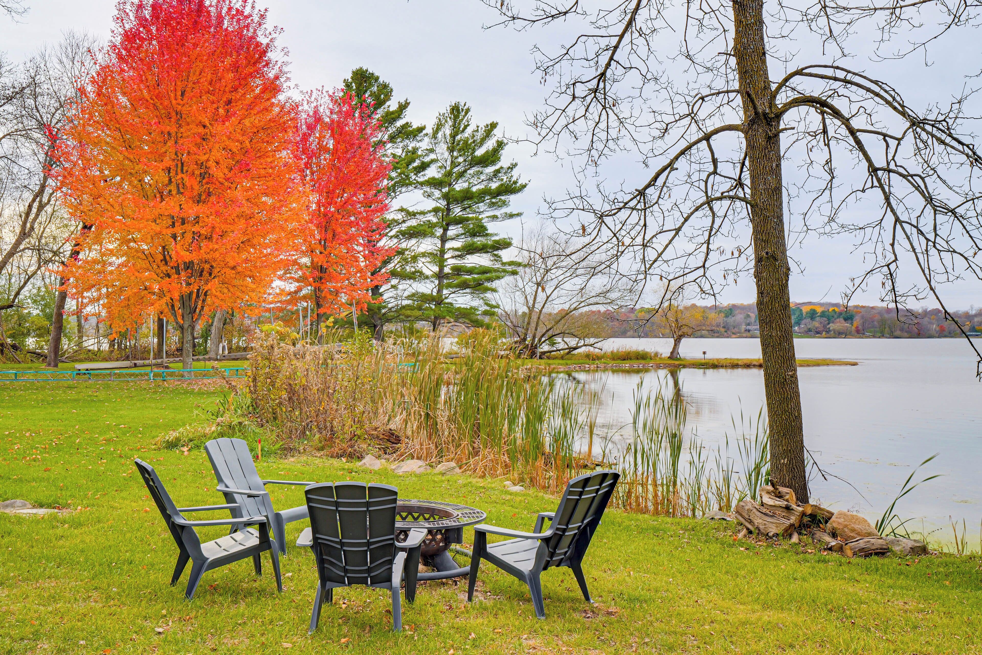 A lakeside setting with a fire pit and chairs.