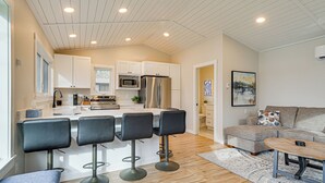 A modern kitchen with white cabinets, a central island with bar stools, stainless steel appliances, and a dining area with a sofa and coffee table. - Fish, Swim & Explore! 2-cabin Camp on Round Lake (Luck)
