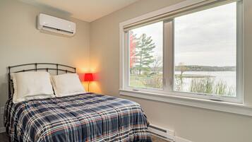 A bedroom with a bed, a window with a view of a lake, an air conditioner, and a red lamp.