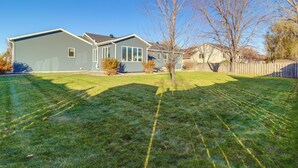 A residential house with a well-maintained lawn, a wooden fence, and a clear blue sky. - Work & Play: Pet-friendly Fargo Home 6 Mi to Dtwn (Fargo)