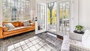 Ein geräumiges Wohnzimmer mit großem Fenster, einer Couch, einem Sessel und einem kleinen Tisch mit einer Pflanze.