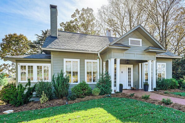 A two-story house with a front porch, a chimney, and a well-maintained garden. - Main Street Elkin Retreat: Home w/ Backyard Oasis (Elkin)