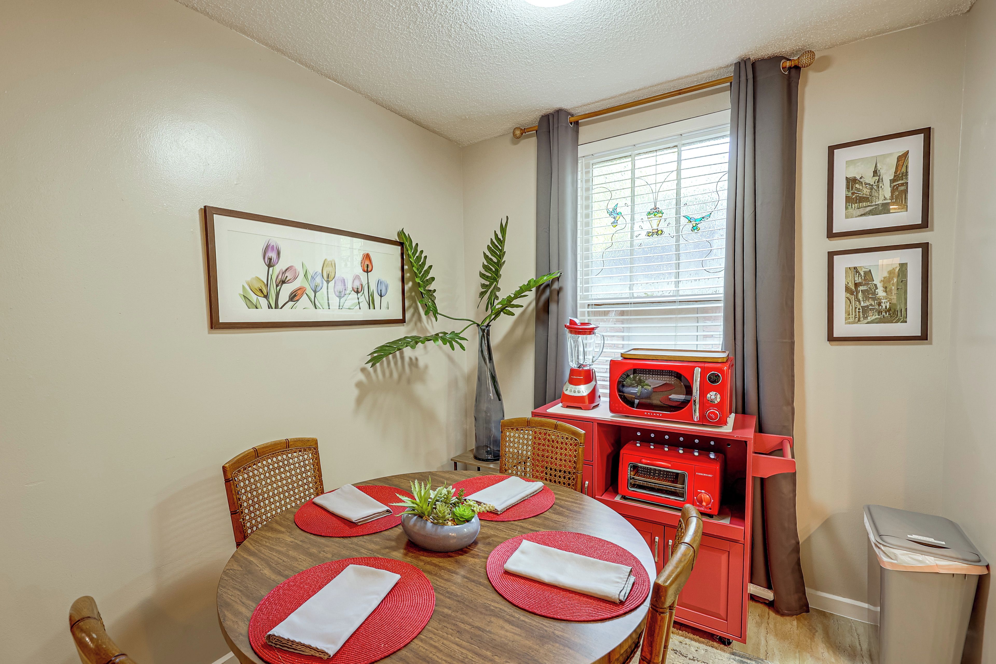 A dining area with a wooden table, red placemats, and a red appliance unit.