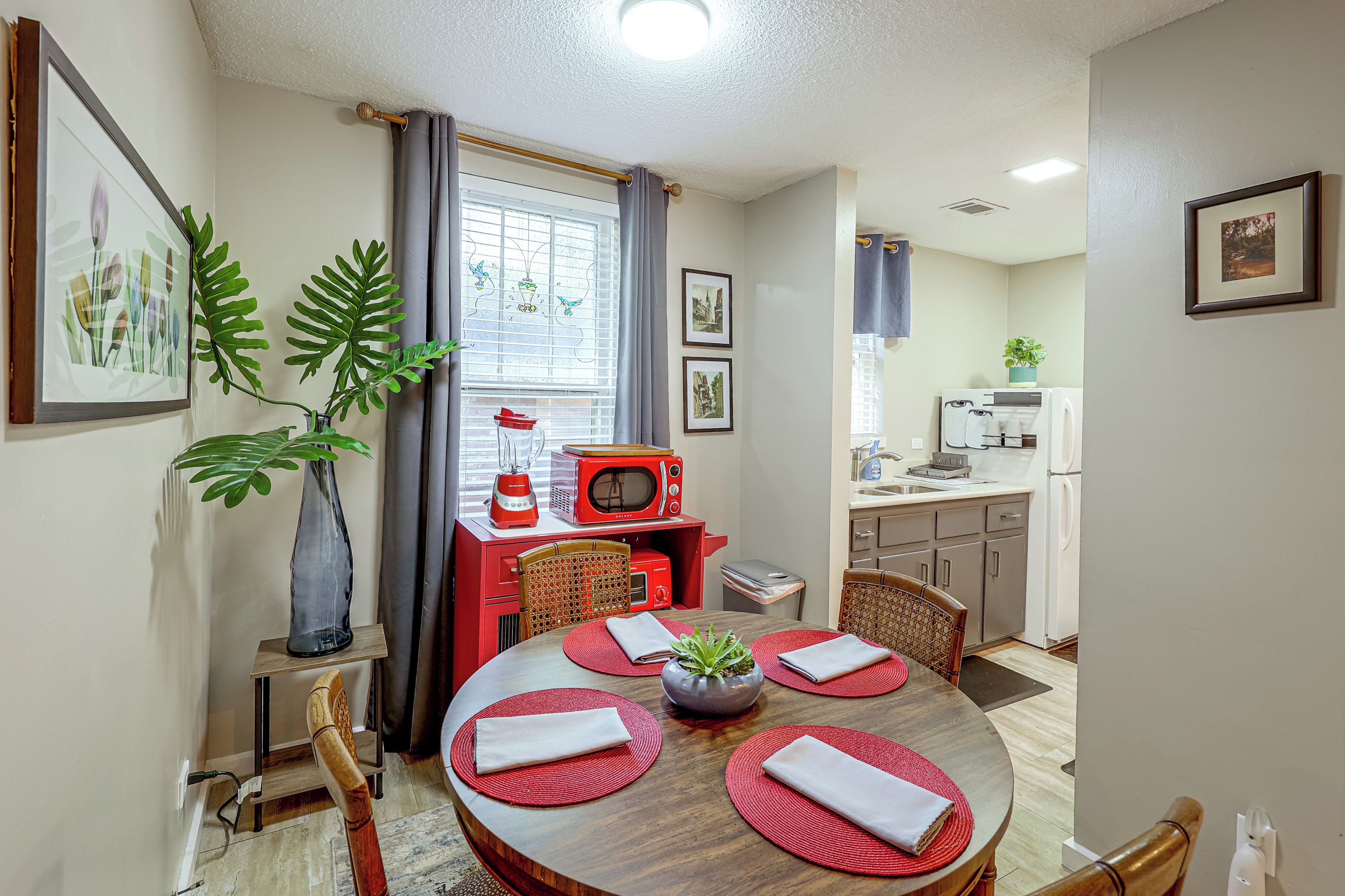 A compact kitchen with a dining area, featuring a red microwave, a sink, and a window with curtains.