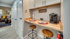 Et lille køkken med hvide skabe, en træbordplade og to barstole.