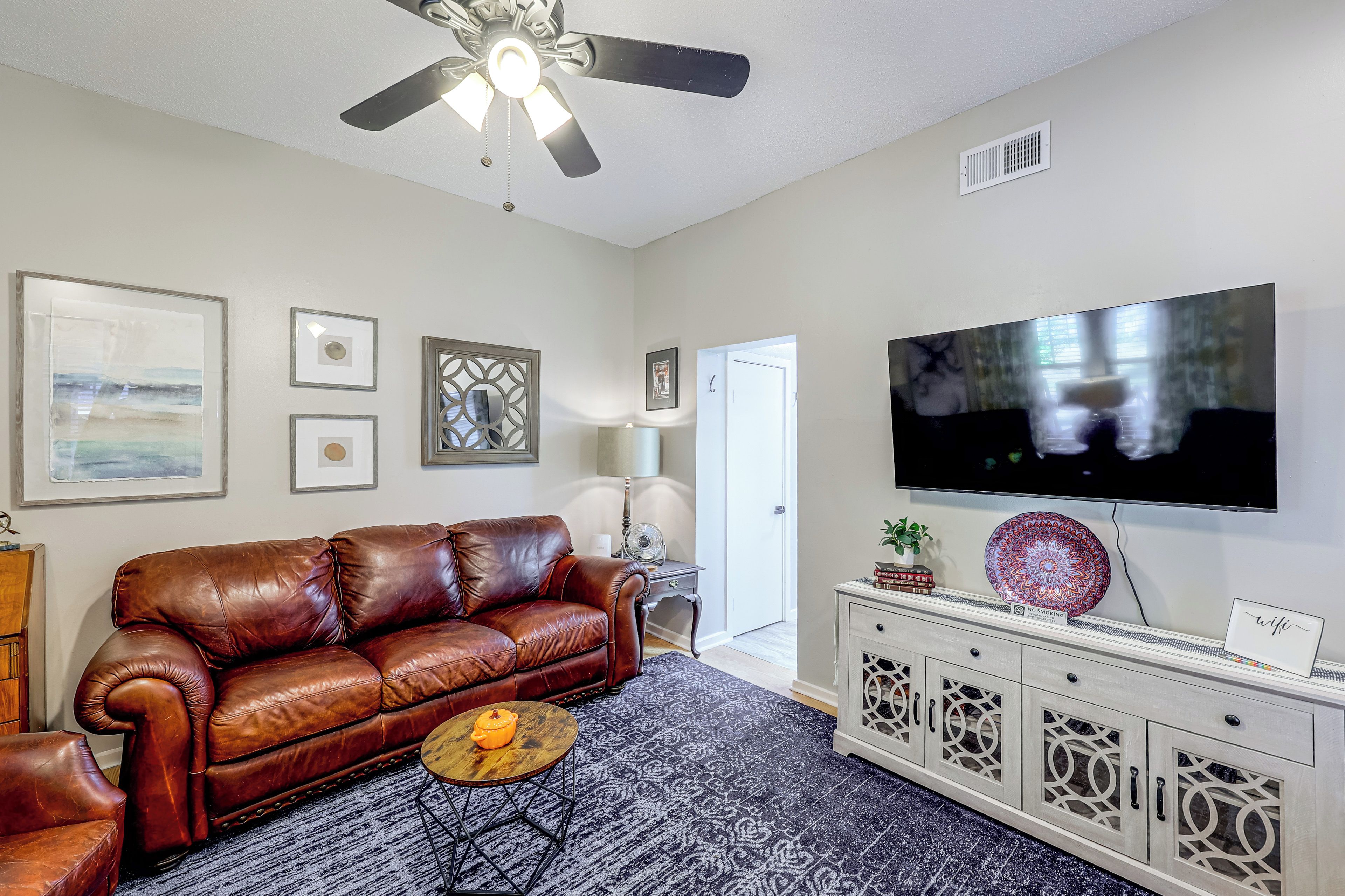 A living room with a brown leather sofa, a flat-screen TV, decorative wall art, and a patterned rug.