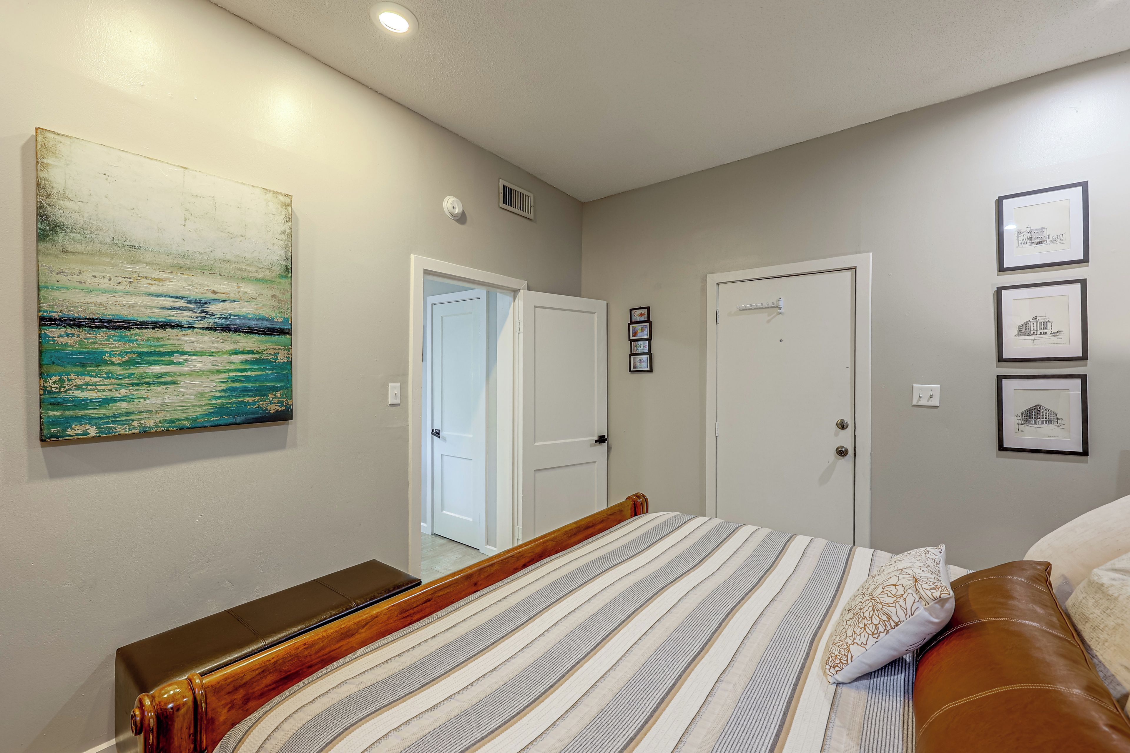 A bedroom with a bed, a nightstand, a painting, and a door.