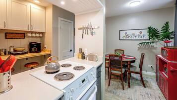 A modern kitchen with white cabinets, a stove, and a dining area with a red cabinet and a framed picture on the wall.