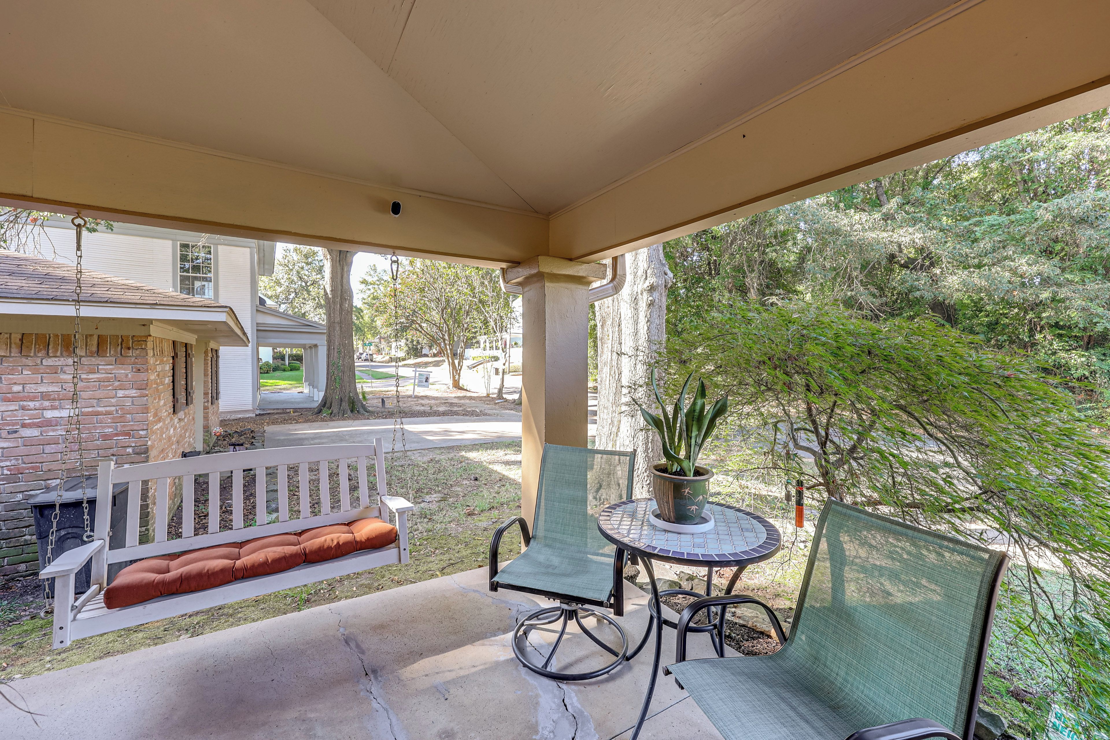 A covered patio with a swing, a table with chairs, and a potted plant.