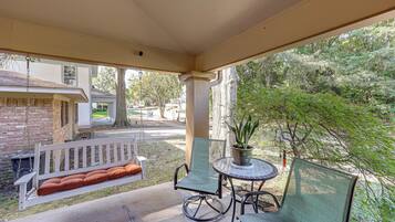 A covered patio with a swing, a table with chairs, and a potted plant.