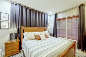 A bedroom with a wooden bed, a nightstand, a lamp, a bedside table with a candle, and a window with blinds. - < 1 Mi to Dtwn Texarkana: Couple's Retreat w/ Yard (Texarkana)