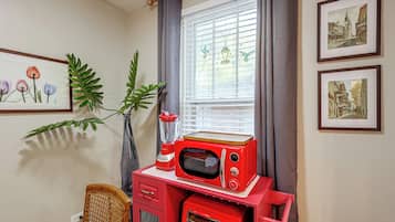 A kitchen with a red appliance, a window with blinds, and framed artwork on the wall.