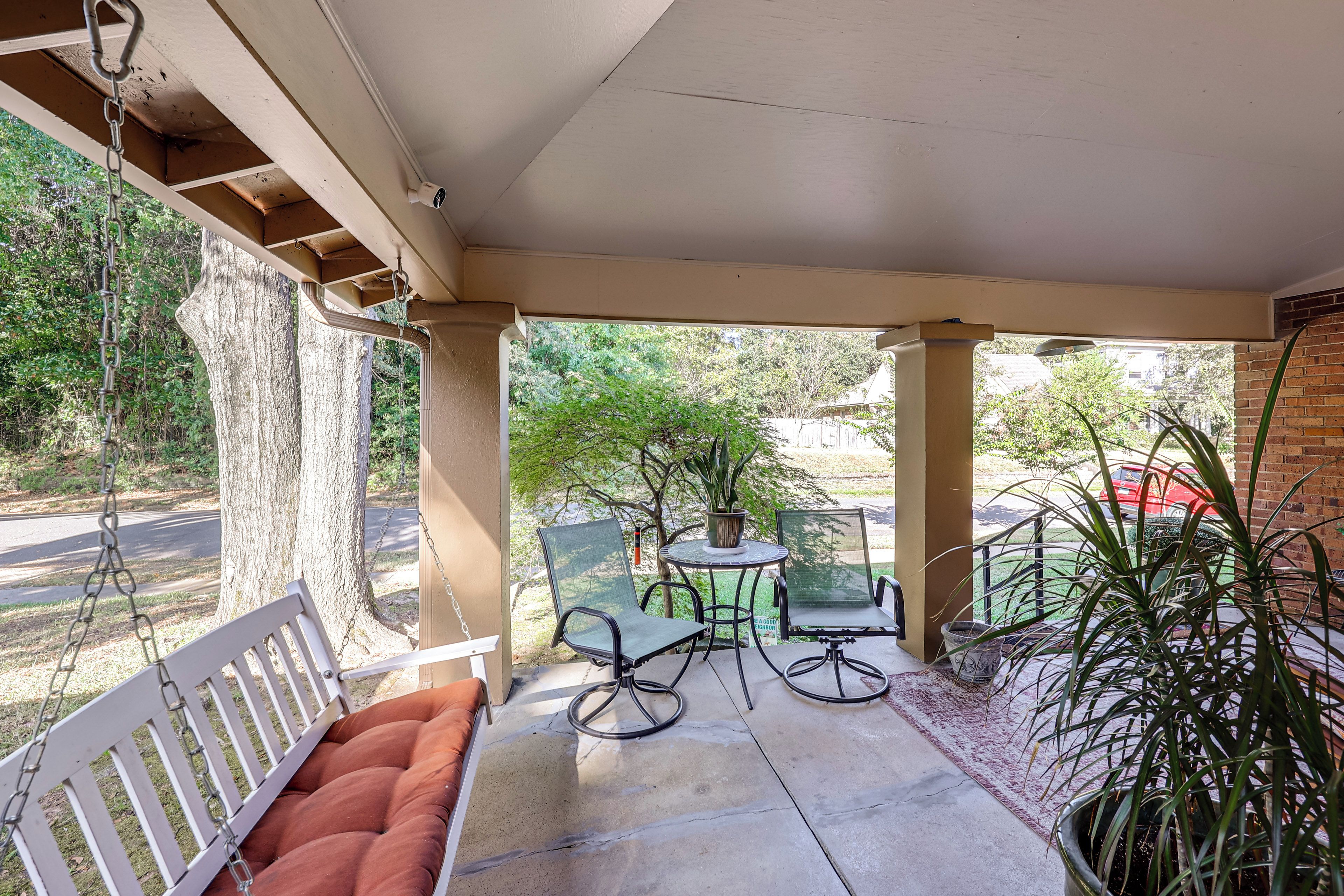A covered patio with a swing set, seating, and potted plants.