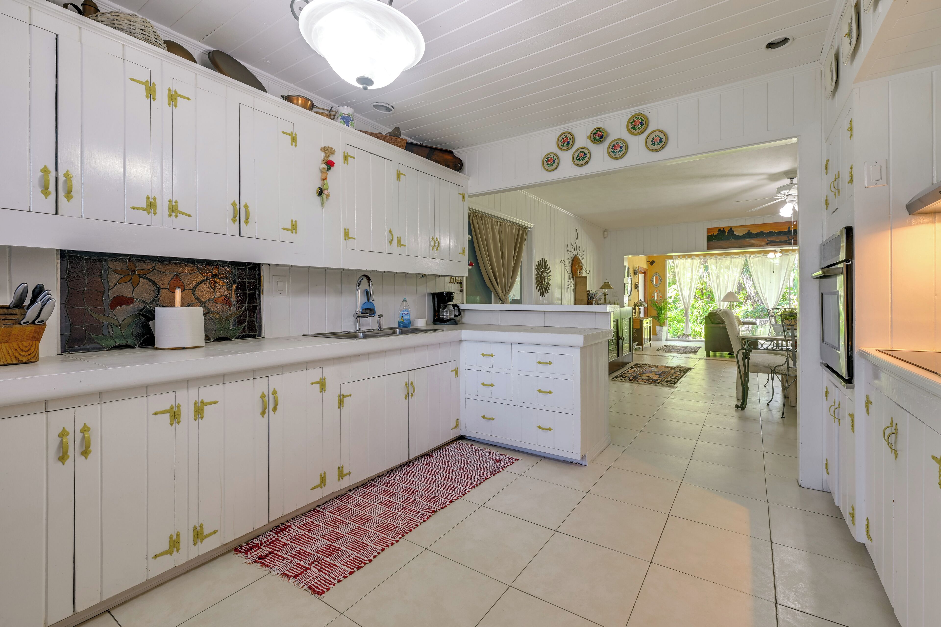 A kitchen with white cabinets, a red rug, and a dining area visible in the background.