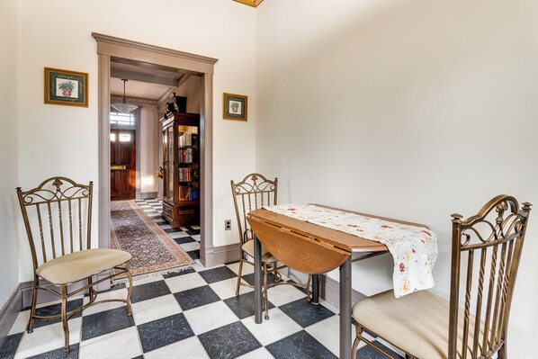 A dining area with a checkered floor, a table with a floral tablecloth, and two chairs.