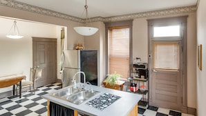 A kitchen with a checkered floor, a central island with a sink, a refrigerator, and a window with blinds. - Pet-friendly Historic Library Home on Route 66 (Virden)
