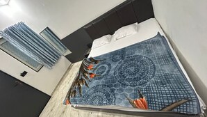 A bed with a patterned bedspread, a window with curtains, and a dark headboard. - R.K Hotel & Restaurant (Khatoo)