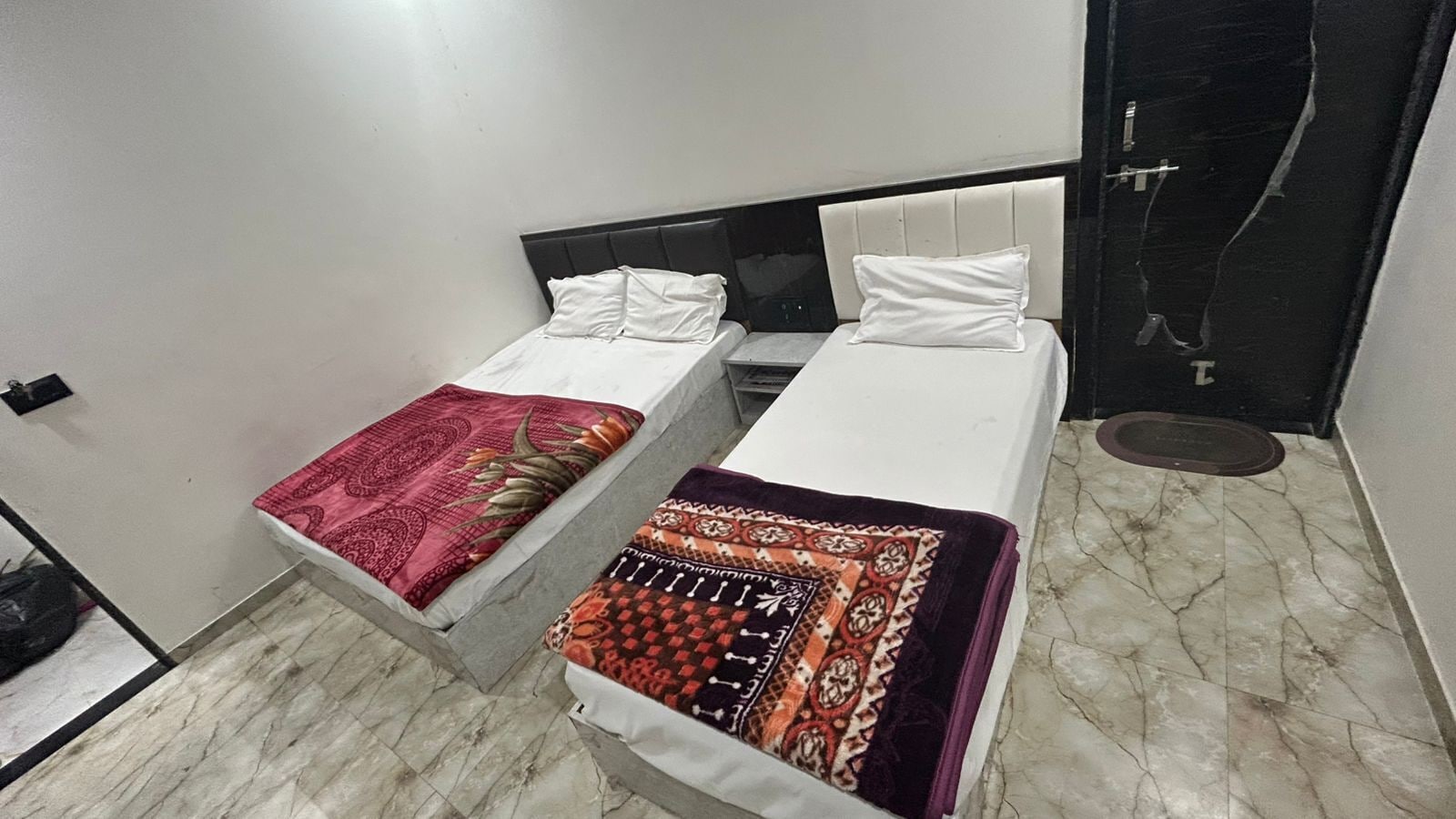Una habitació amb dos llits individuals, cadascun amb un estovat estampat. La habitació té un paviment de marbre i una porta negra.