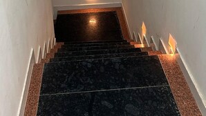 A narrow stairway with a black and brown marble floor, white walls, and a small light at the top. - R.K Hotel & Restaurant (Khatoo)