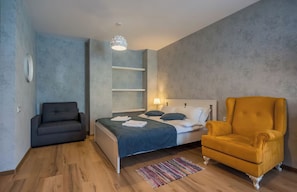A bedroom with a bed, a sofa, a chair, and a hanging light fixture. - New Gudauri Loft 🏂⛷️ (Gudauri)