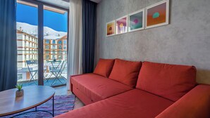 Ein modernes Hotelzimmer mit einem roten Sofa, einem kleinen Tisch mit einer Pflanze und Blick auf schneebedeckte Gebäude durch große Fenster.