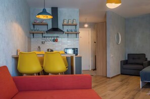 Ein kompakter Wohnbereich mit Küchenzeile, einem Essbereich mit gelben Stühlen, einem roten Sofa und einem dunkelgrauen Sofa.