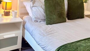 Un letto rifatto con cuscini bianchi e verdi, un comodino con una lampada e uno specchio rotondo appeso al muro.