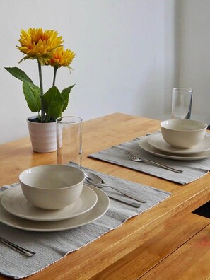 A dining table set with white bowls, plates, and cutlery, accompanied by a glass and a potted plant with yellow flowers. - Modern 2 bed flat in City Centre, High speed WiFi (Cardiff)
