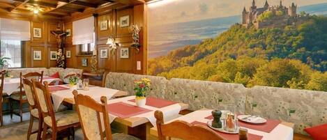 A dining area with wooden tables and chairs, a mural of a castle on a hill, and a view of the landscape.