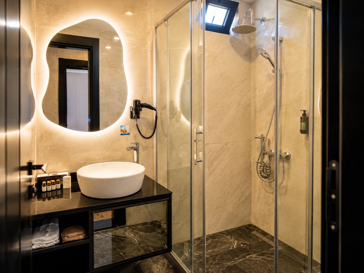 Un baño moderno con ducha envuelta en vidrio, un espejo redondo y un tocador con lavamanos y artículos de aseo.