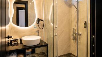Un baño moderno con ducha envuelta en vidrio, un espejo redondo y un tocador con lavamanos y artículos de aseo.