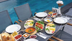 A dining table set for a meal with various dishes, including salads, bread, and a hot plate, overlooking a swimming pool. - ROSSA MARIN HOTEL (Darica)