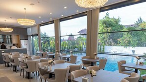 A modern dining area with tables and chairs, a pool, and large windows overlooking a garden. - ROSSA MARIN HOTEL (Darica)