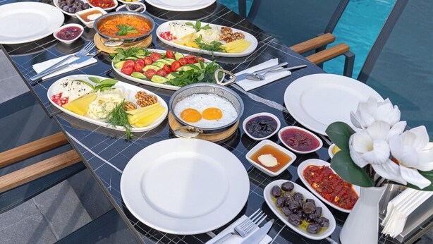 A dining table with a variety of dishes, including eggs, salads, and bread, set up by a poolside with a clear view of the water. - ROSSA MARIN HOTEL (Darica)