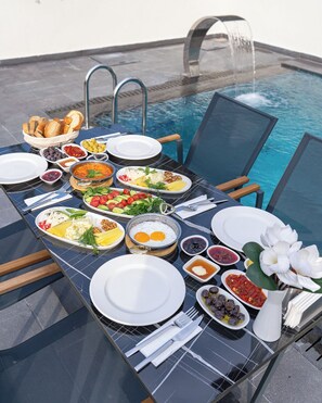 A dining table with a variety of dishes, including eggs, salads, and bread, set up by a poolside with a clear view of the water. - ROSSA MARIN HOTEL (Darica)