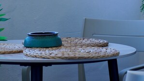 Ein runder Tisch mit einer gewebten Tischmatte, einer türkisblauen Vase und einem Stuhl mit einem blumigen Sitzkissen.