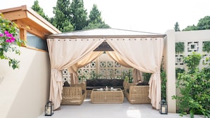 A covered outdoor seating area with wicker furniture and a table set for two. - THE GARDEN Bise (Motobu)