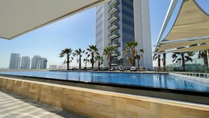 Un espace aménagé au bord de la piscine, offrant une vue sur les gratte-ciel, les palmiers et les chaises longues.