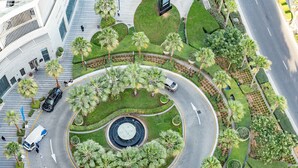 Une route circulaire bordée de palmiers, avec une fontaine au centre, le tout entouré de verdure et de bâtiments.