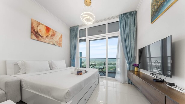 Une chambre d’hôtel moderne dotée d’un grand lit, d’une télévision à écran plat, d’un coin repas et d’un balcon offrant une vue sur la ville.