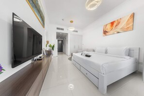 Ein modernes Hotelzimmer mit großem Flachbildfernseher, einem Bett mit weißen Bettwäsche, einem Holztischchen und einem Gemälde an der Wand.