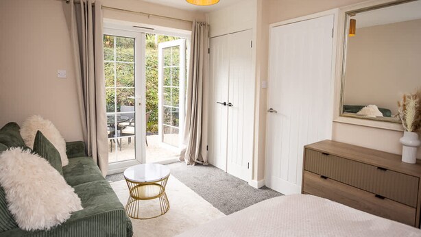 A bedroom with a green sofa, a round coffee table, a bed, a dresser, and a sliding glass door leading to an outdoor area. - Rose Cottage - 2 Bedroom Cottage - Penally (Tenby)